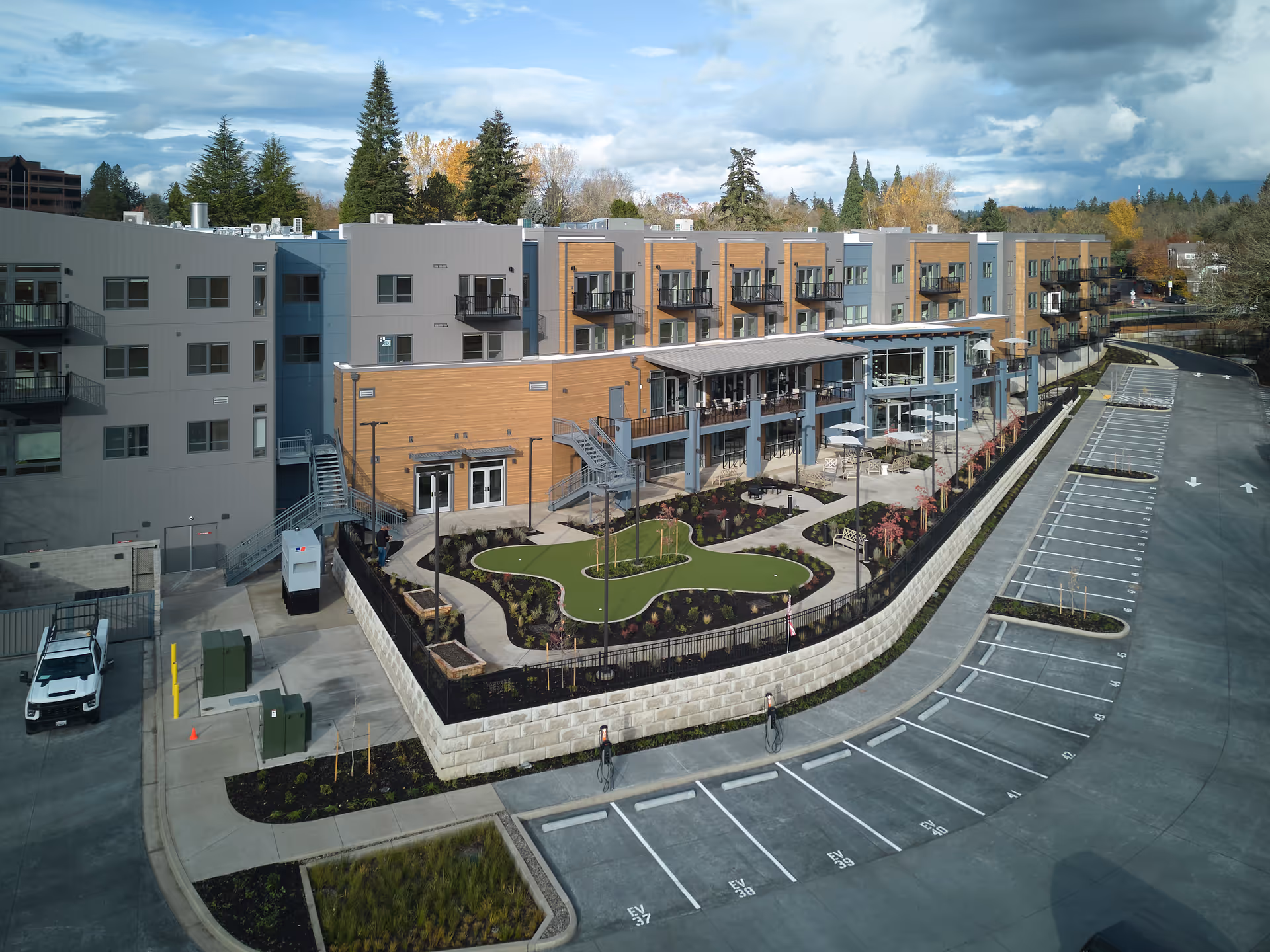 Exterior view of the Cogir of Tigard senior living building with a landscaped courtyard, balconies, and a large adjacent parking lot.