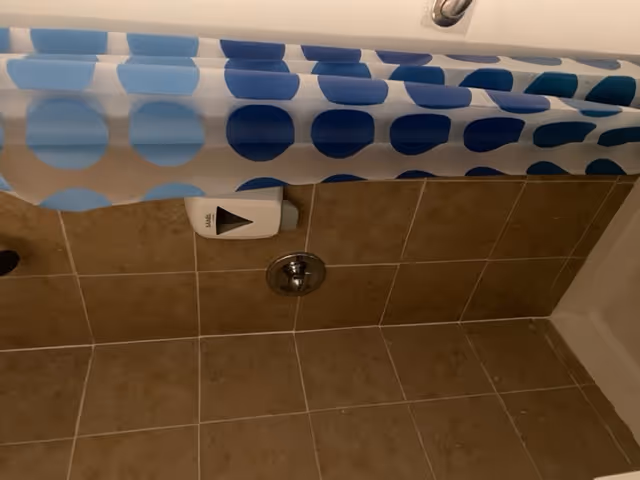 Tiled bathroom with a blue polka-dot shower curtain and visible toilet paper dispenser.