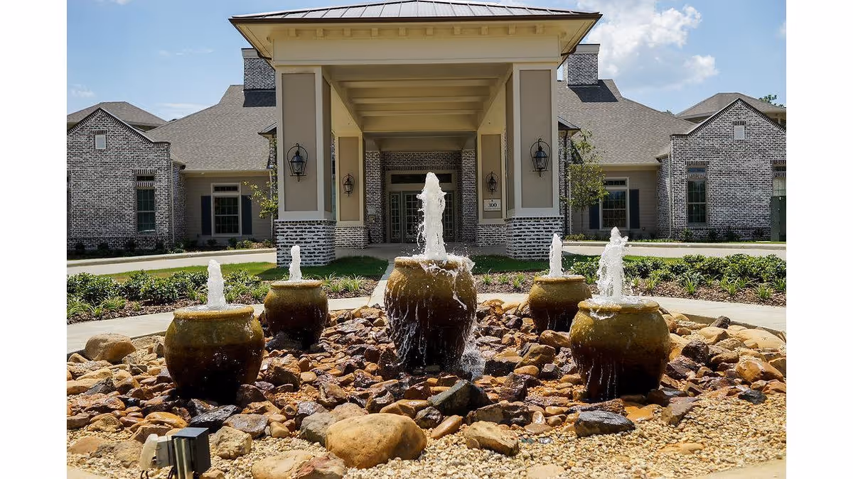 Front entrance of a brick building featuring a covered porte-cochère, a five-urn fountain, and landscaped circular driveway.