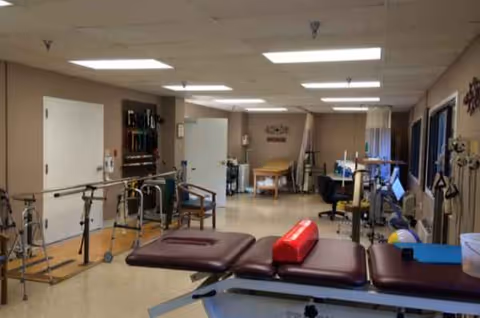 Interior rehabilitation gym with therapy tables, parallel bars, and exercise equipment.
