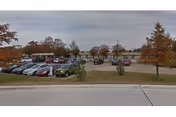 Wide view of the Cypress Point Nursing & Rehabilitation Center building with a parking lot in front. Several cars are parked, and there are trees with autumn foliage around the area under a cloudy sky.