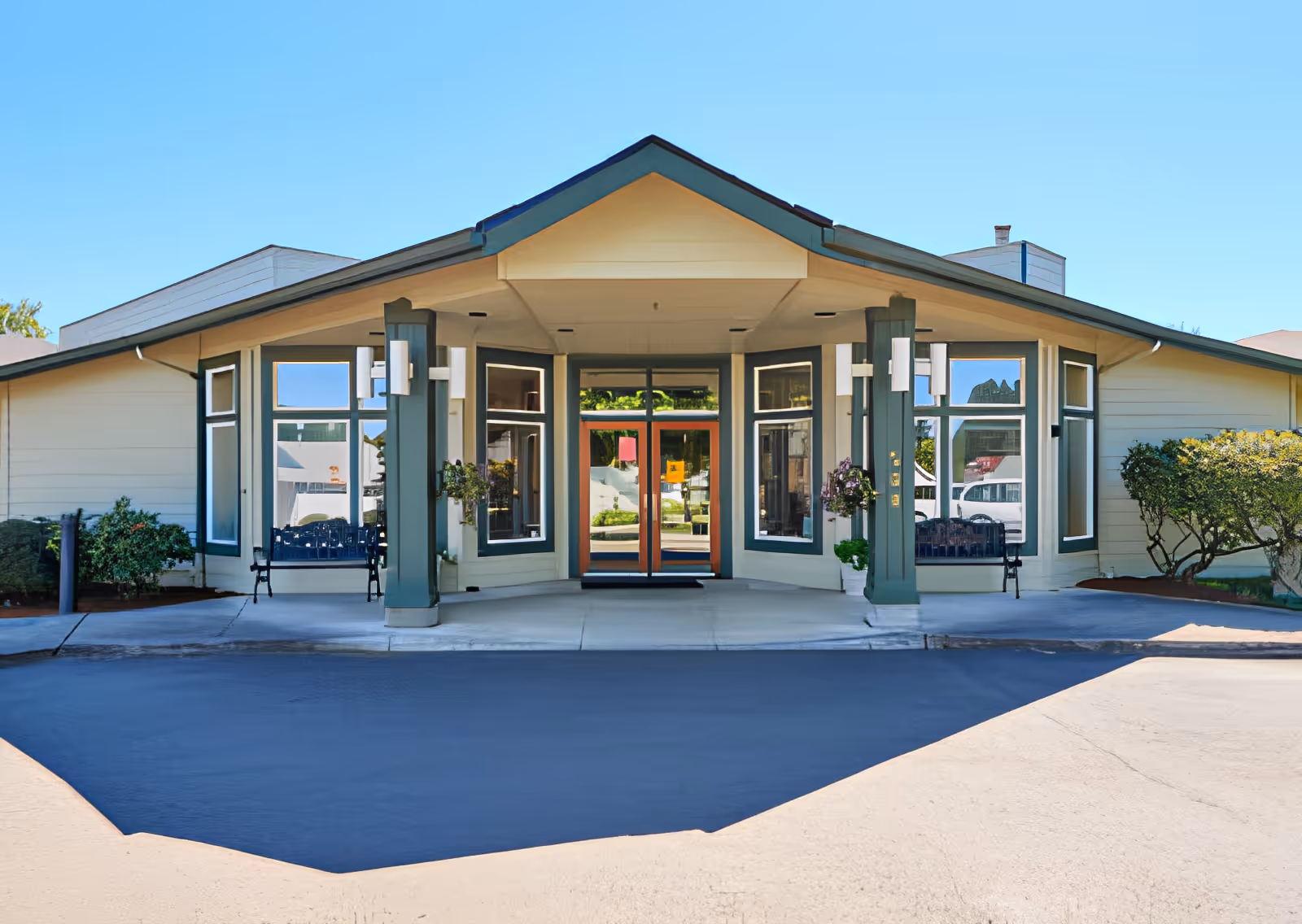Exterior front entrance of the Elliott Residence with a covered entry, pillars, large windows, and surrounding shrubs.