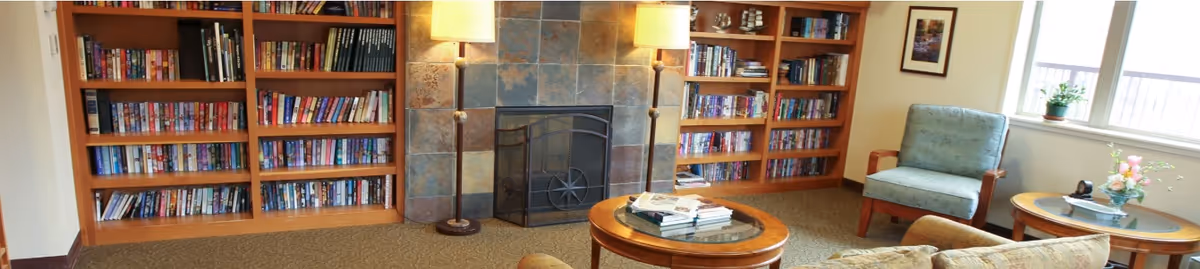 Cozy common room with built-in bookshelves, a tiled fireplace, armchairs and coffee tables.