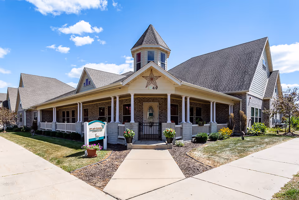 Front exterior of a senior living facility with a wraparound porch, central turreted entrance, and landscaped walkway.