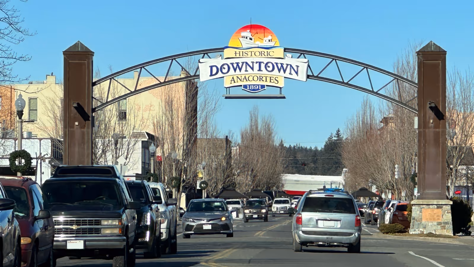 Historic downtown arch sign reading 'Downtown Anacortes' spans a busy street with parked cars.