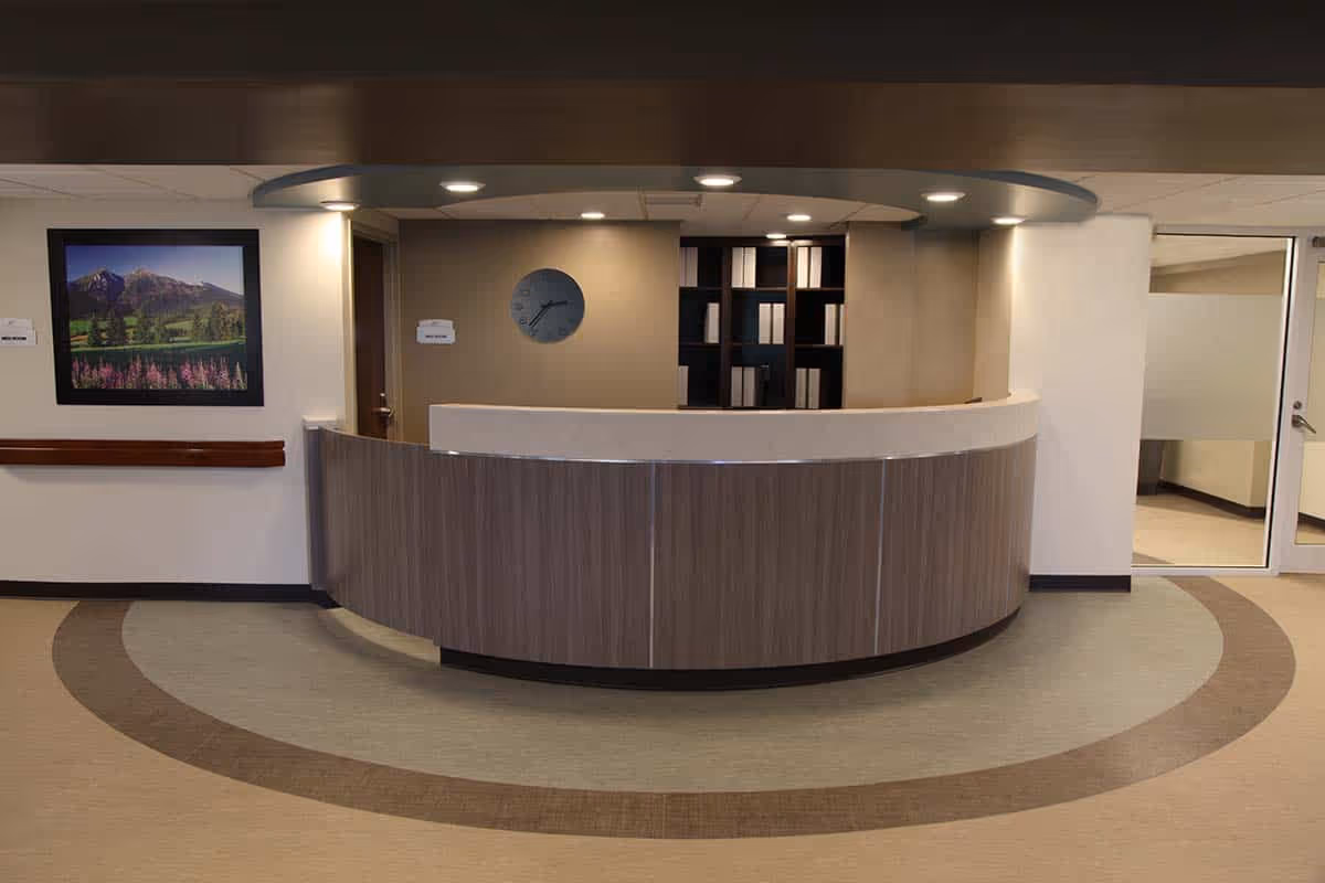 A curved reception desk in a modern lobby with a circular floor pattern, a wall clock, and framed landscape art.