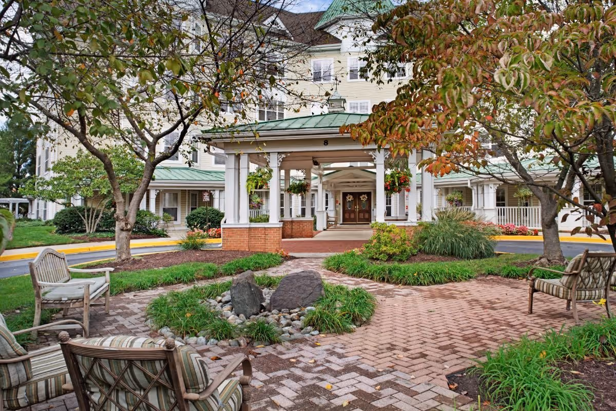 Front entrance of Sunrise of Rockville senior living facility with a covered porte-cochère, landscaped courtyard, and outdoor seating.