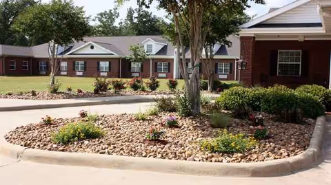 Brick senior living facility with manicured landscaping and curved stone-edged garden beds near the entrance.