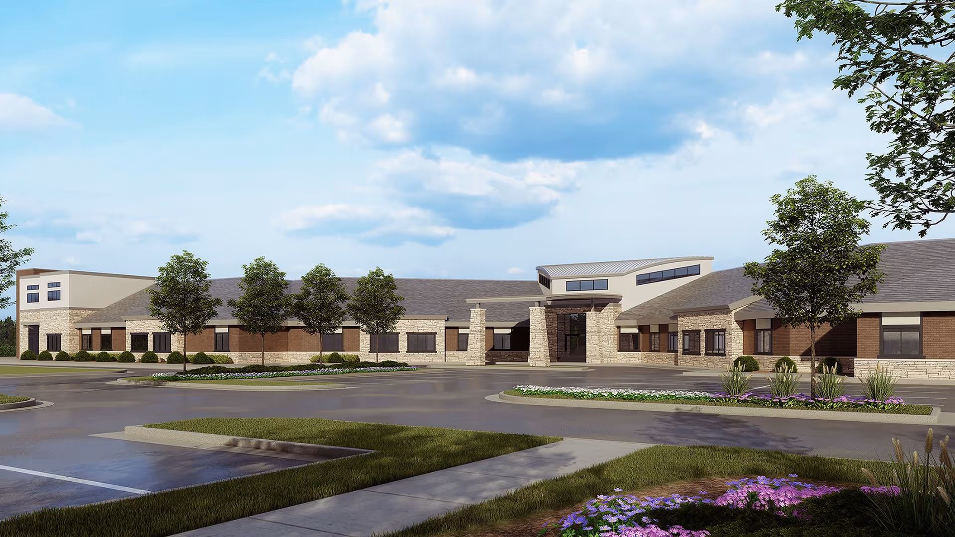 Exterior view of a single-story senior living facility building with a combination of brick and stone facade, multiple windows, and a covered entrance. The surrounding area includes a parking lot, landscaped greenery, trees, and flower beds under a partly cloudy sky.