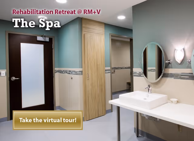 Interior view of a spa area in a rehabilitation retreat at Rochester Manor + Villa, featuring a white sink with a mirror above it, a wooden door, and a frosted glass door. The walls are painted teal and beige with decorative tile accents.