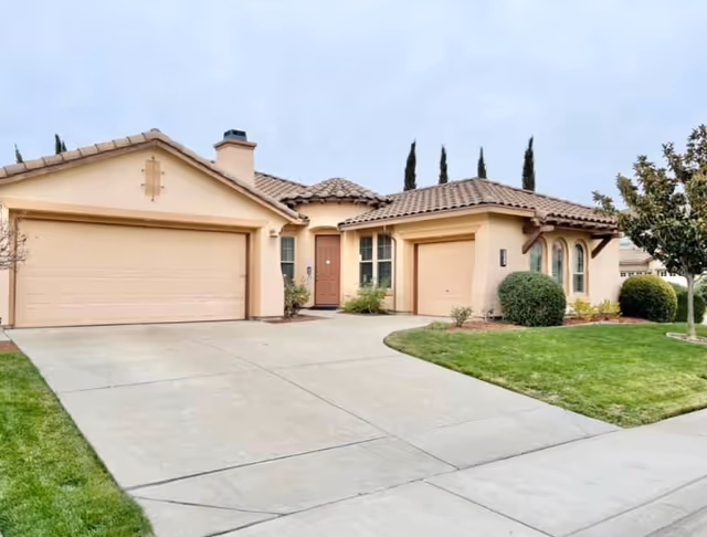 Beige stucco senior care home's front exterior featuring a three-car garage and manicured lawn
