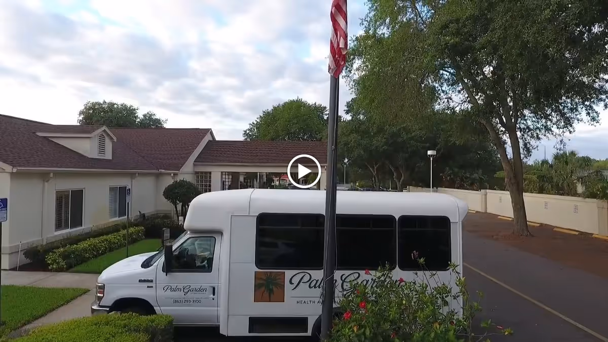 A Palm Garden shuttle van parked in front of a single-story senior living building with a flagpole and trees.