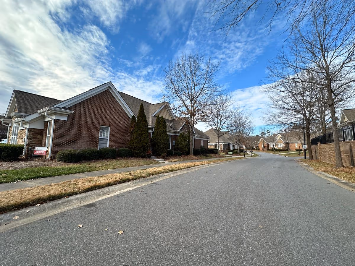 Street view of brick single-story villas along a curved road with leafless trees under a partly cloudy sky.