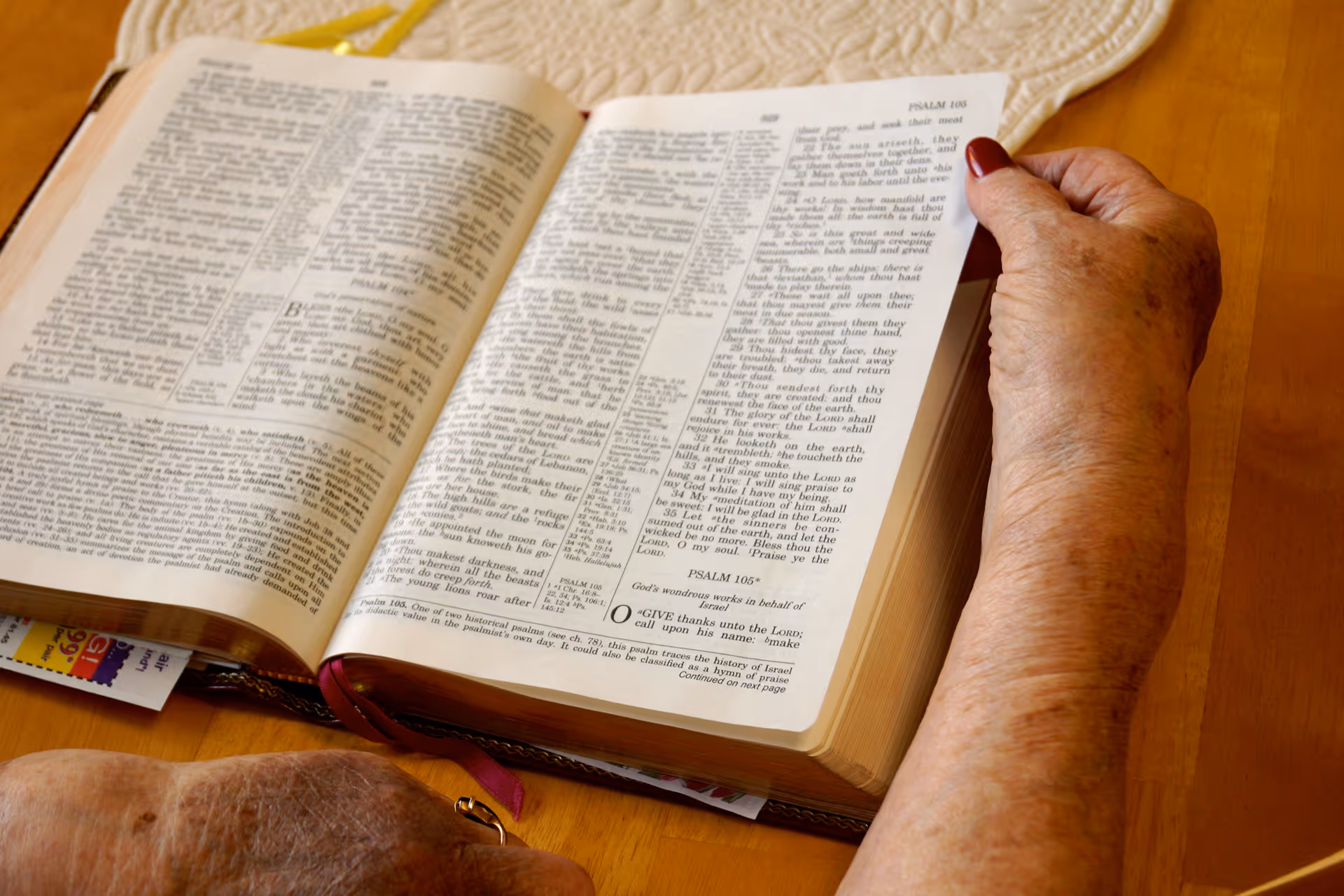 An elderly person's hands holding open a Bible on a wooden table.