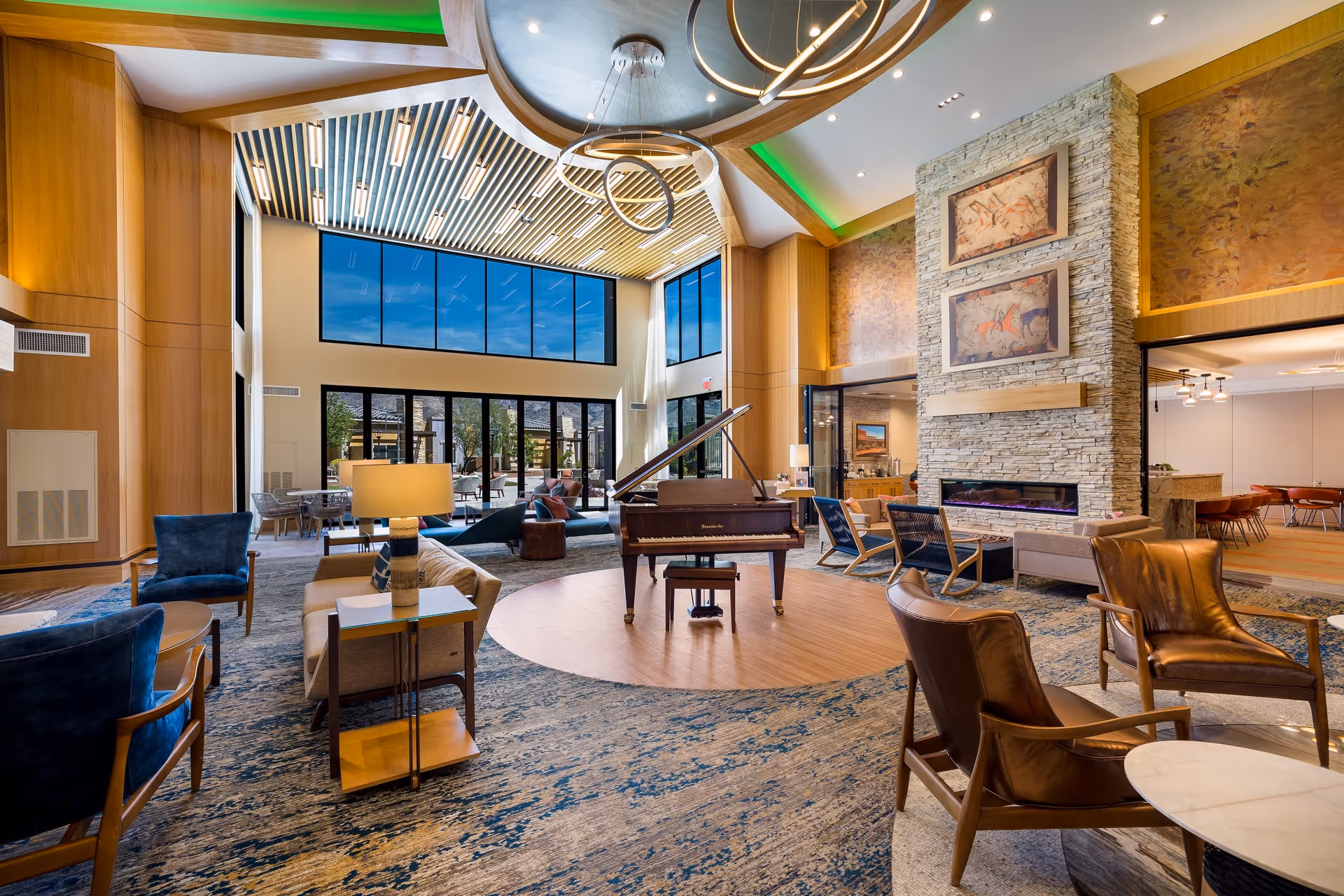 Spacious senior living lounge with a grand piano, multiple seating areas, a stone fireplace, and large windows.
