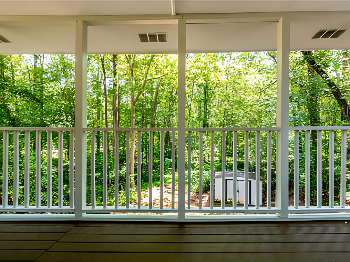 Covered porch with white railing overlooking a lush, tree-filled backyard.