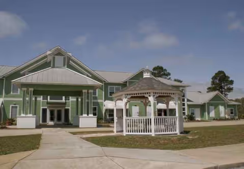 Exterior view of a green senior living facility with a white gazebo in front.