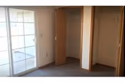 Empty room with beige carpet, two open wooden closets, and a sliding glass door leading to an outdoor area.
