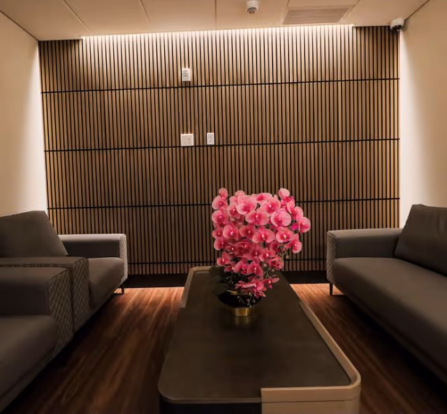 Modern lounge with two gray sofas facing a central coffee table holding a pot of pink orchids in front of a slatted wooden accent wall.