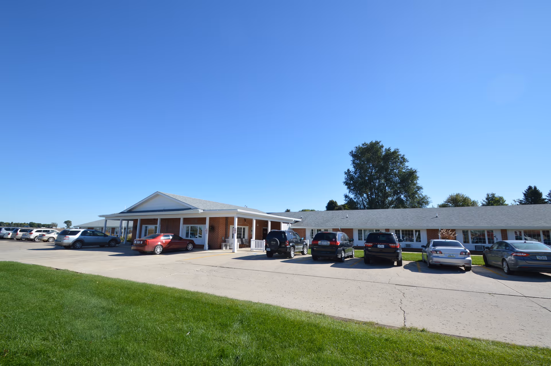 Single-story brick care facility with a covered entrance and several parked cars under a clear blue sky.