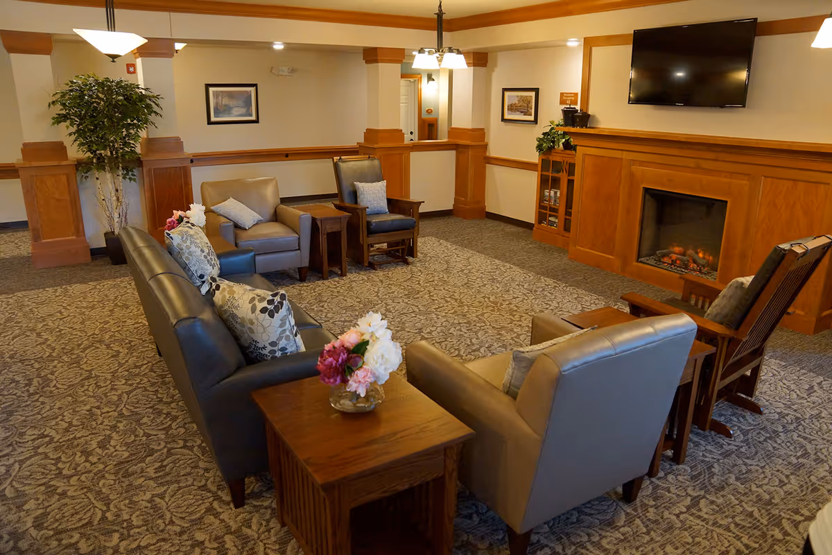 Comfortable seating area in a senior living facility with sofas, armchairs, a fireplace and a wall-mounted TV.