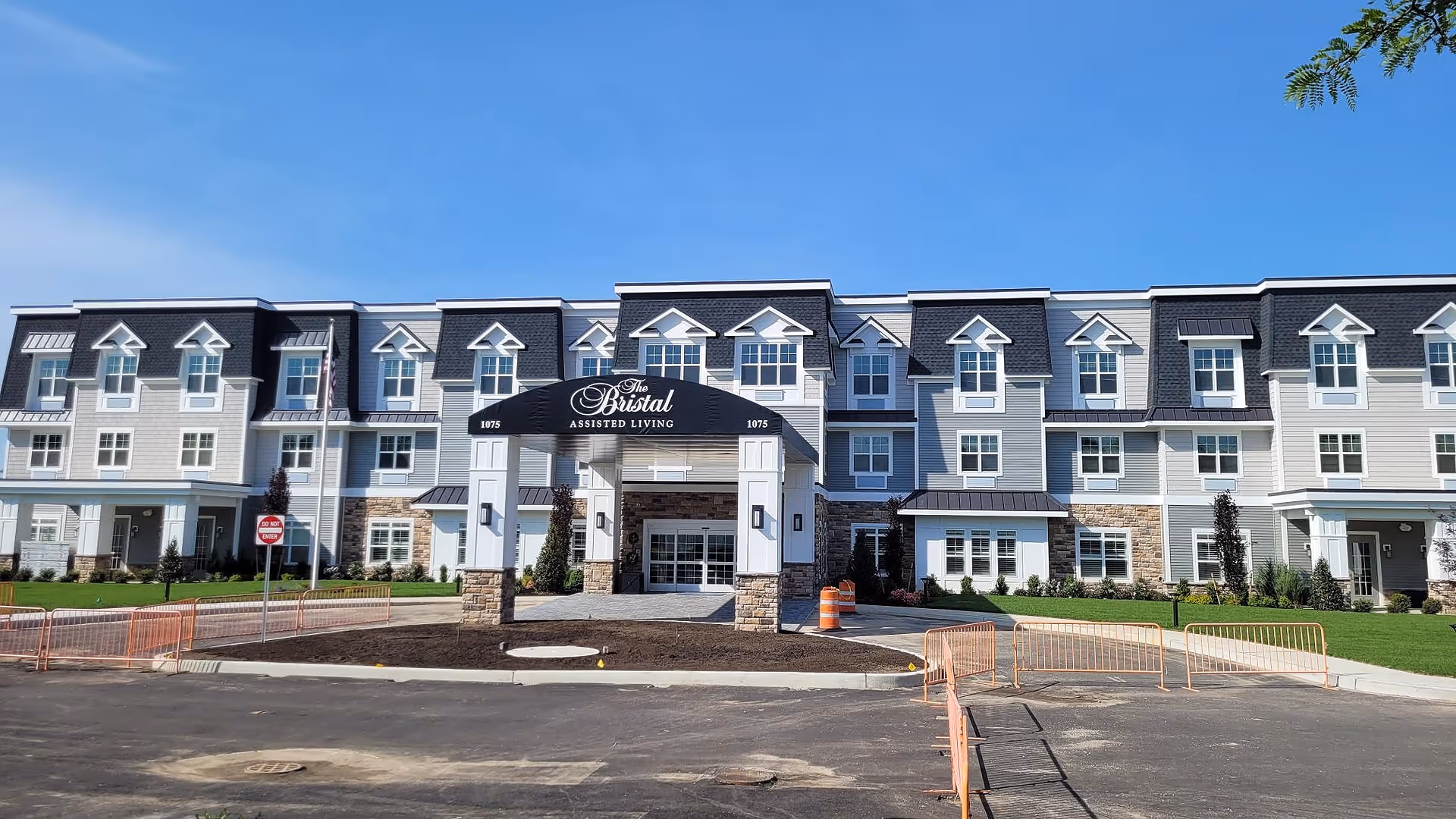 Front exterior of The Bristal Assisted Living building showing a three-story facade, covered entrance canopy with signage, and paved driveway.