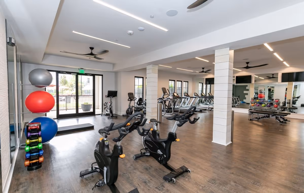 Bright fitness center with exercise bikes, treadmills, weight rack, and exercise balls in a spacious room.