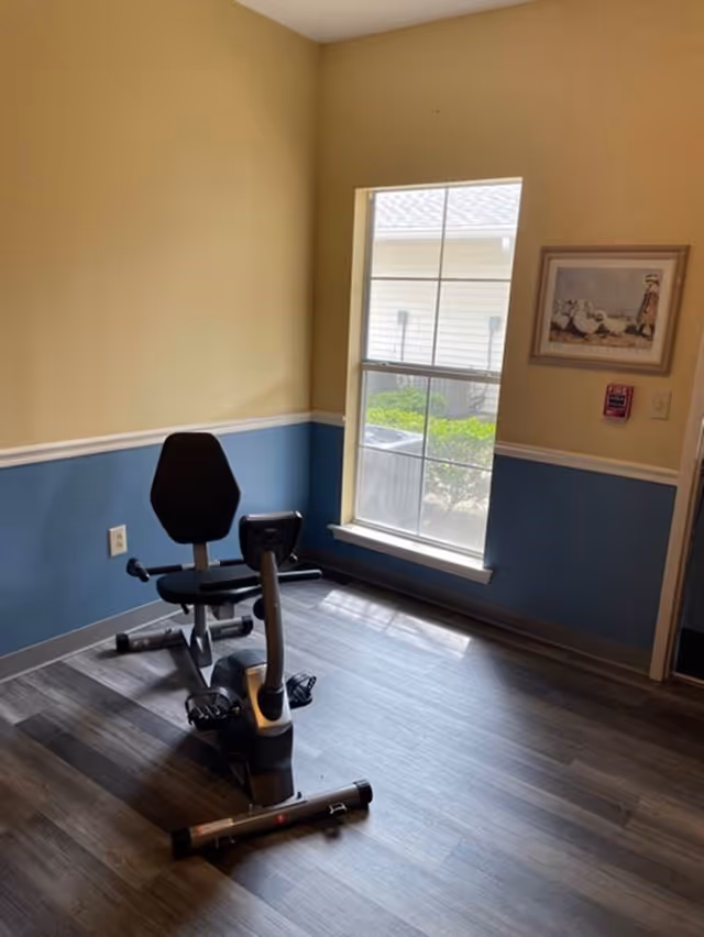 Small interior room with a recumbent exercise bike near a window, wood-look flooring, and two-tone painted walls.