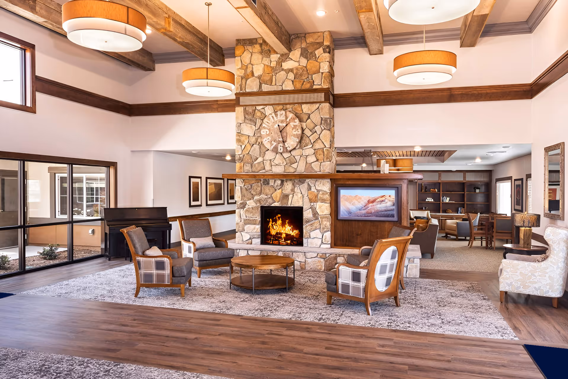 A spacious communal lounge with a central stone fireplace, comfortable armchairs, a TV, and exposed wooden beams.