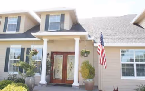 Front view of a residential senior living facility entrance with columns, plants, and an American flag.