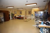 Rehabilitation therapy room with parallel bars, treatment tables, exercise equipment, and seating.