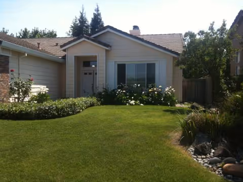 Front view of a single-story house with a green lawn and shrubs.