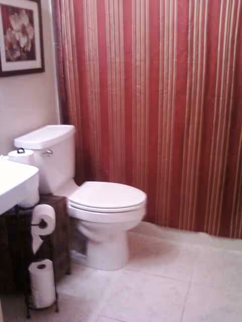 A bathroom with a white toilet beside a sink and striped red wallpaper.