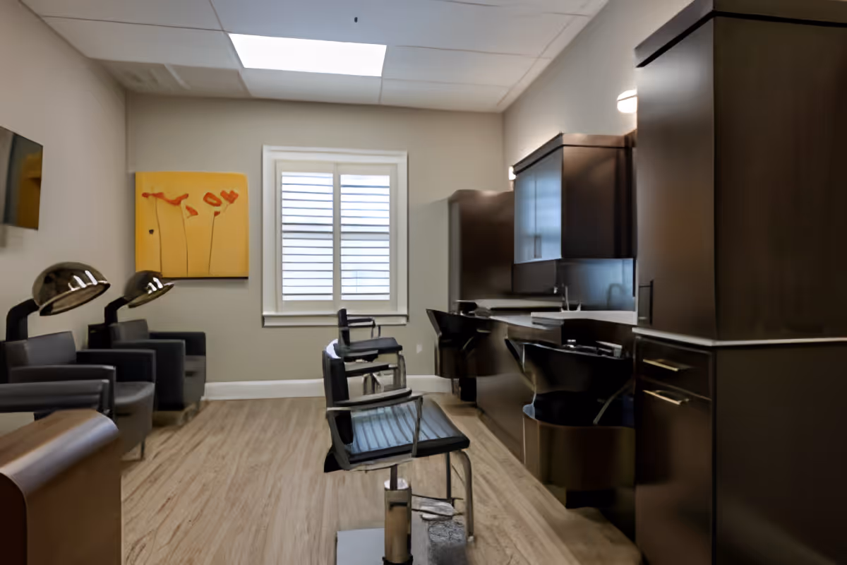 Interior salon room with barber chairs, hair-washing sinks, hooded dryers, and dark cabinetry.