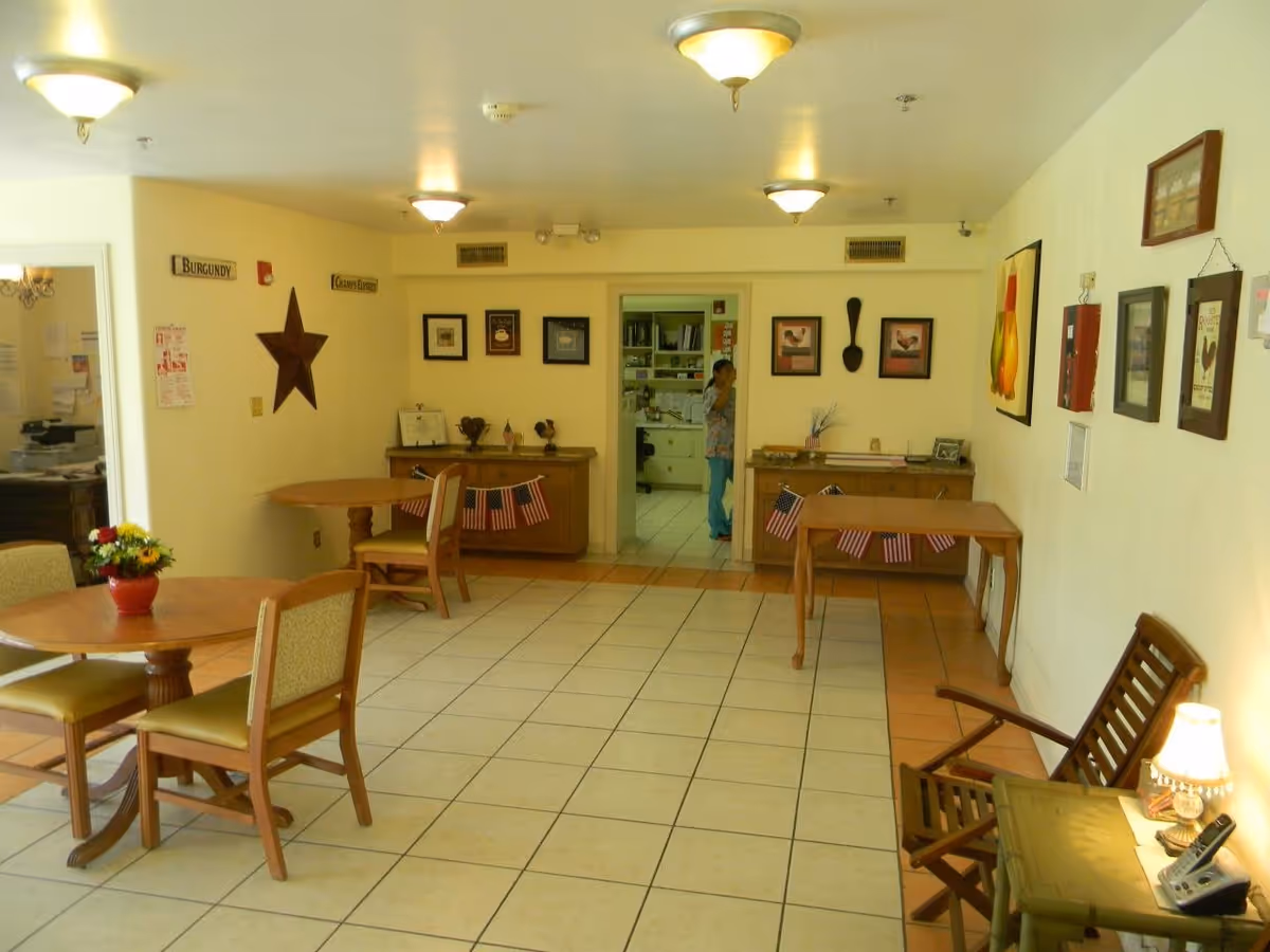 Communal dining/lounge area with round tables and chairs, wall decorations, and a staff member visible in a doorway.