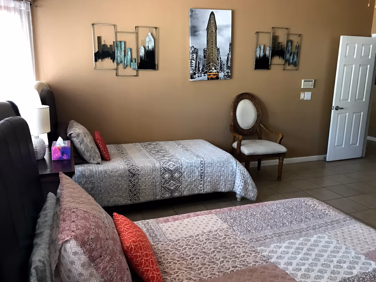 A tidy bedroom with two beds, decorative pillows, wall art, a chair, and an open door.
