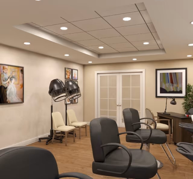 Interior of a salon area in a senior living facility with black salon chairs, two hair dryers on stands, beige chairs against the wall, framed artwork on the walls, a wooden floor, and a desk with a lamp and plant near double glass doors.