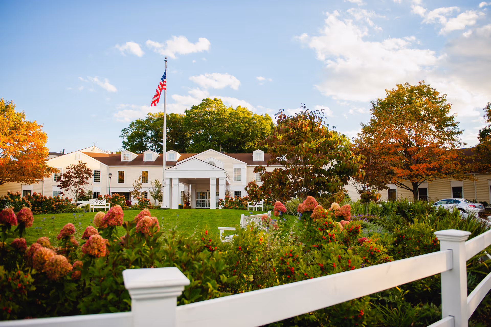 Front entrance of Essex Meadows with landscaped lawn, American flag, and white fence.