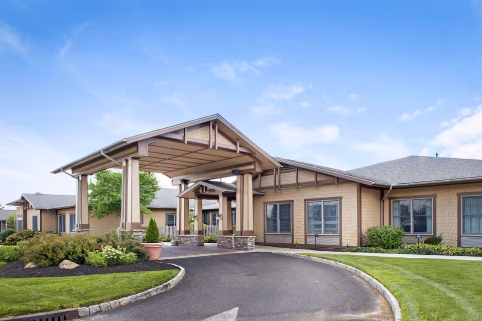 Covered porte-cochère entrance of a single-story senior living facility with landscaped beds and a curved driveway.