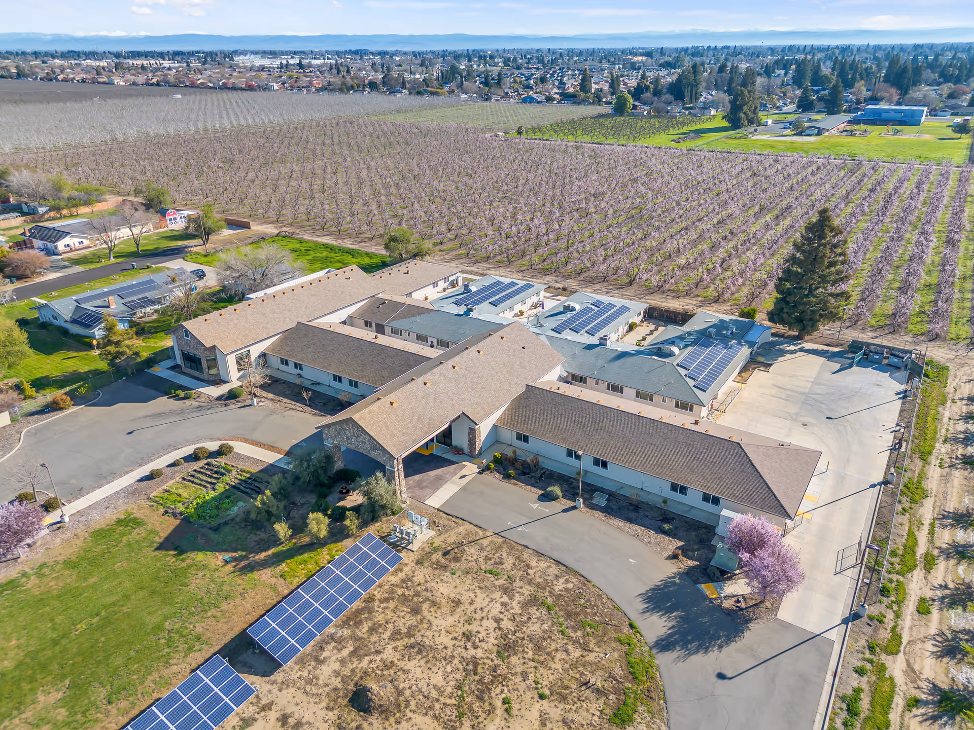 Aerial view of Emerald Oaks Inc showing connected single-story buildings, solar panels, driveways, and surrounding orchards.