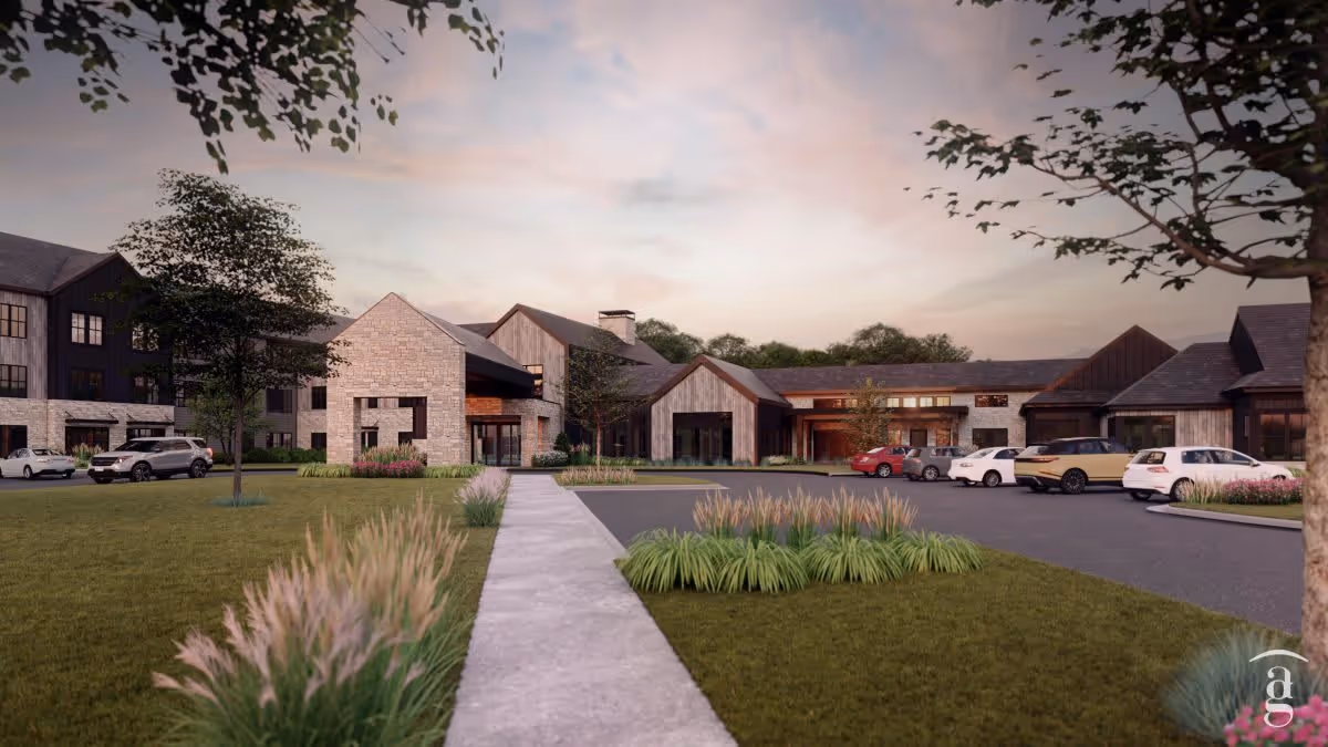 Exterior view of FeatherStone at Hickory Hill facility during sunset, showing a modern building with stone and wood facade, a parking lot with several cars, landscaped greenery, and a concrete walkway leading to the entrance.