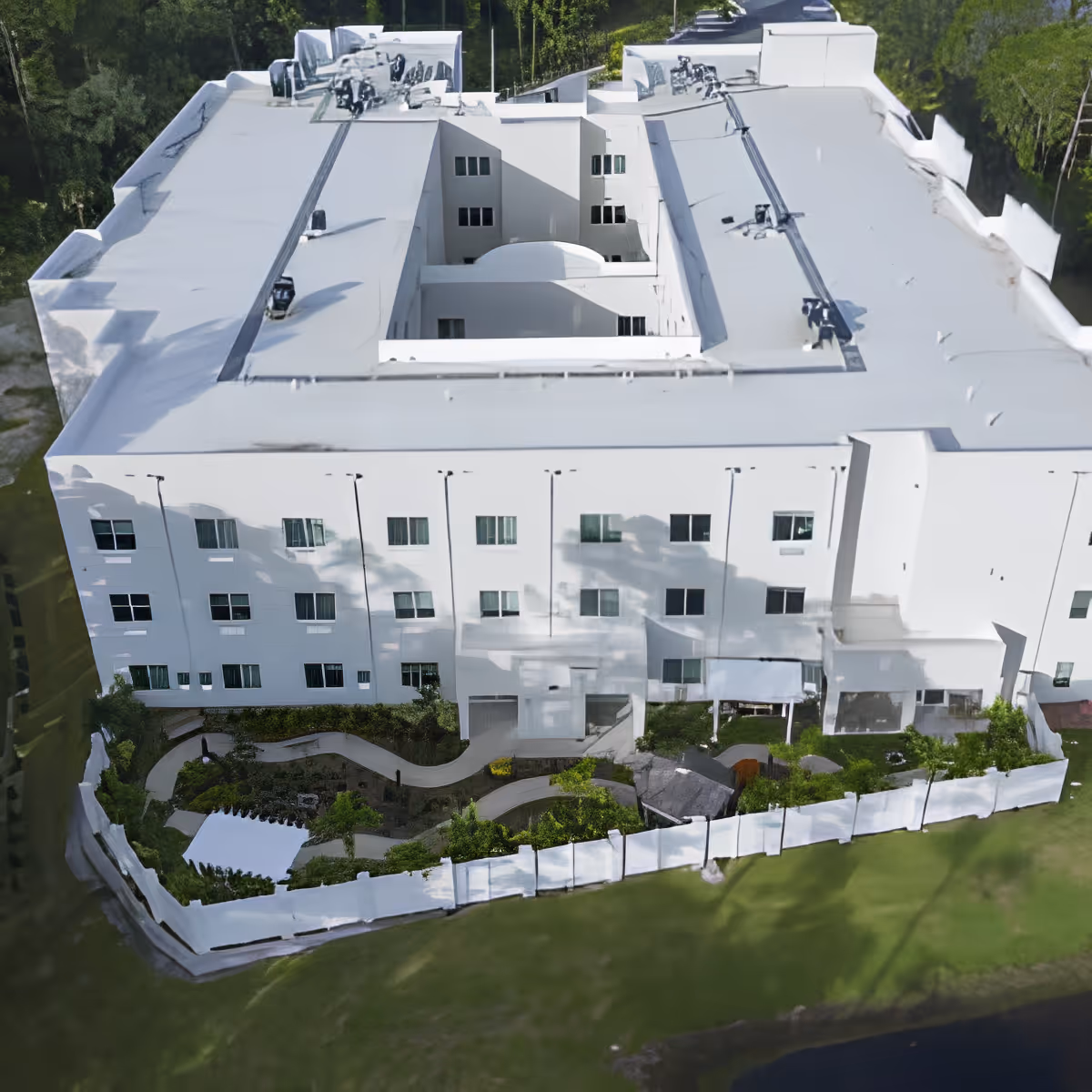Aerial view of a white multi-story senior living building with an enclosed garden courtyard and surrounding fence.