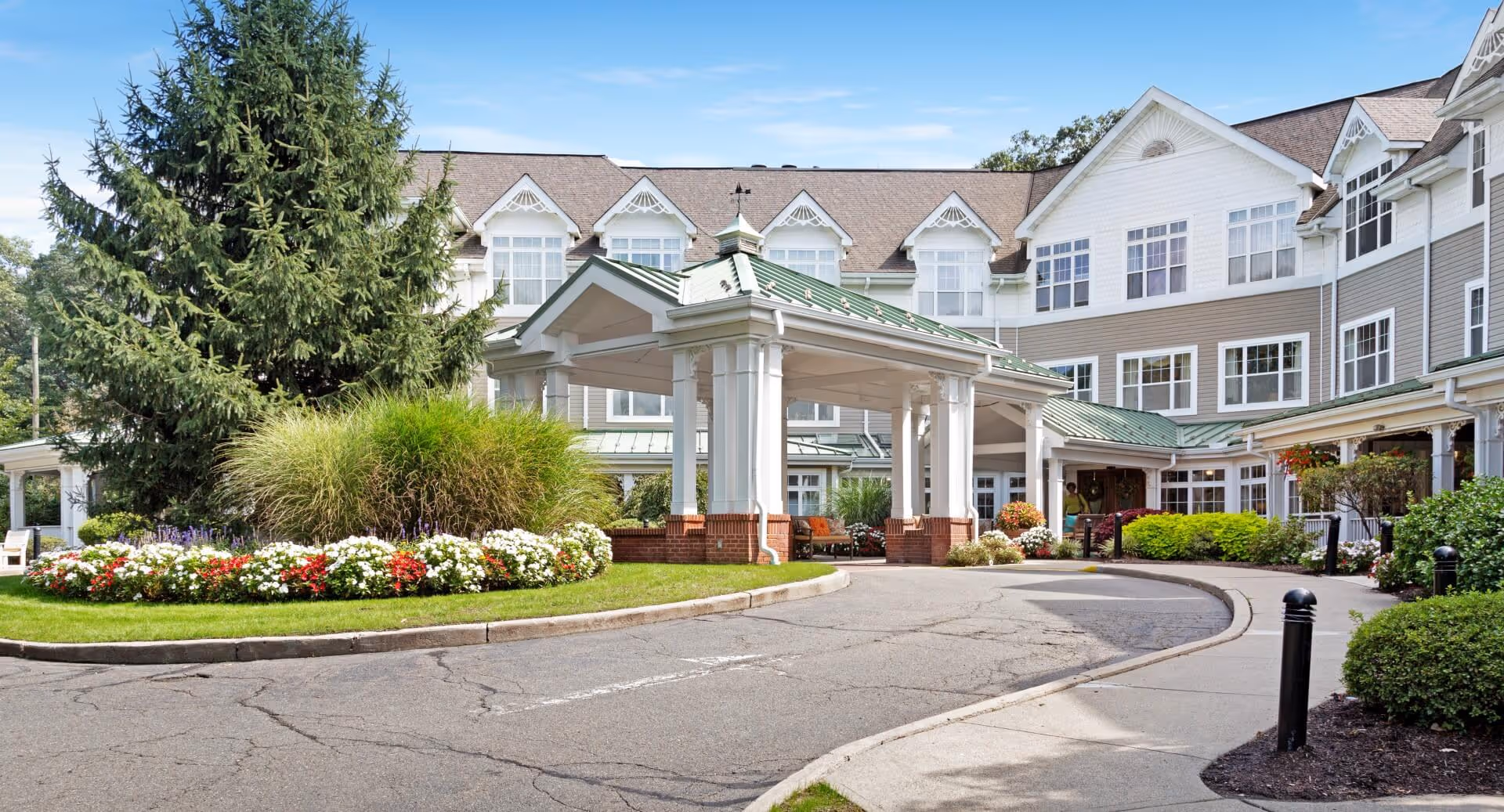 Front view of a senior living facility with covered entrance, curved driveway, and landscaping.