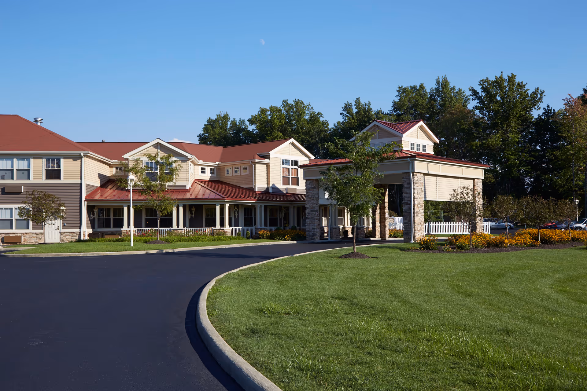 Exterior view of Aberdeen Crossings by New Perspective, showing a large building with beige siding and red roofs, surrounded by green grass, trees, and a curved driveway under a clear blue sky.