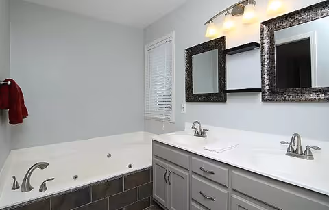 Modern bathroom with a double-sink vanity, two framed mirrors, and a jetted bathtub.