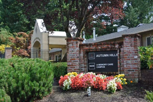 Entrance to Marquis Autumn Hills Residential Memory Care with brick sign and colorful flowers.