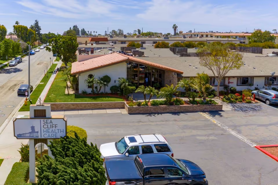 Entrance and parking lot of the Sea Cliff Health Care assisted living building with a sign and landscaping.