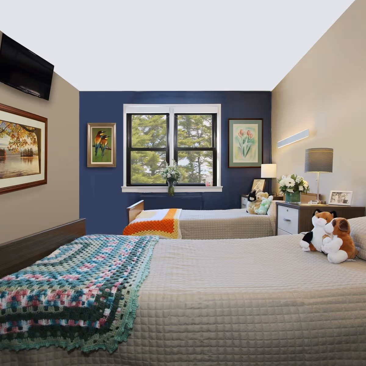 A cozy shared bedroom with two beds, decorative blankets, artwork on the walls, and a window with a view.