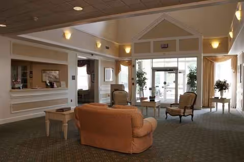 Senior living lobby lounge with beige seating, a reception desk, and glass entrance doors.