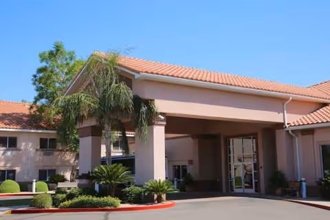 Front entrance of a pink-stucco senior living building with porte-cochere and landscaping.